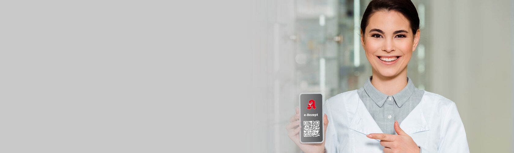 Eine Apothekerin zeigt lächelnd ein Smartphone mit einem E-Rezept-QR-Code in einer modernen Apotheke.