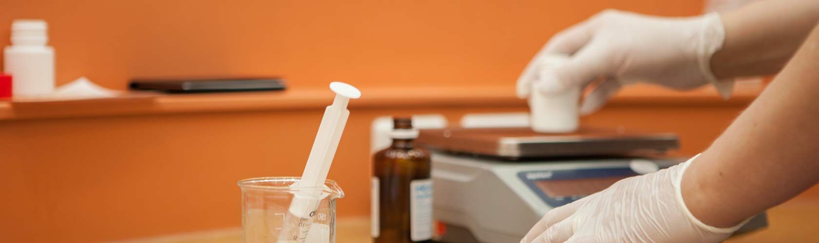 Ein Apotheker mit Handschuhen wiegt Zutaten auf einer Waage in einer Apotheke mit orangefarbenem Hintergrund ab.