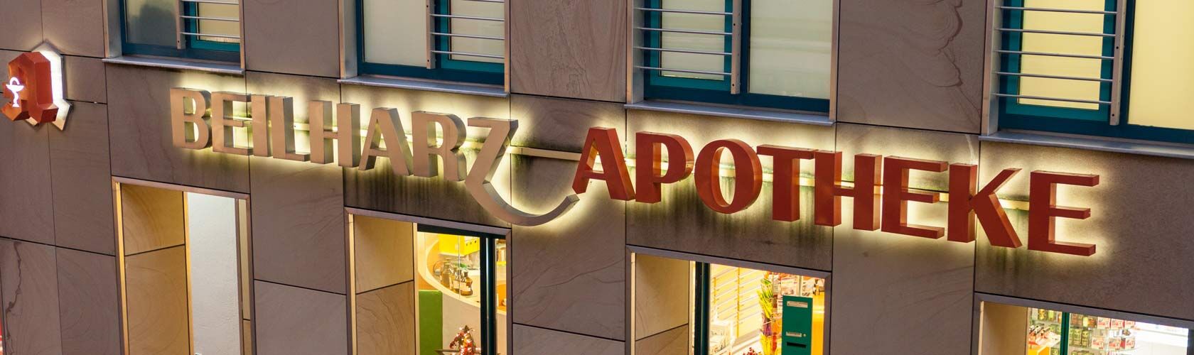 Die beleuchtete Fassade der Beilharz Apotheke in der Wassertorstraße 16 zeigt das markante Apotheken-Logo.