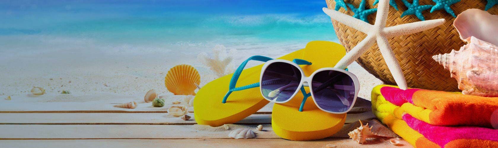 Bunte Flip-Flops, Sonnenbrille und Muscheln liegen auf einem Strandtuch neben einem Strohhut am sonnigen Strand.